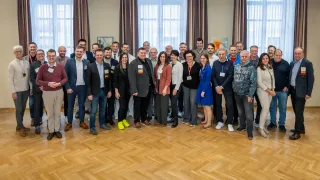 Eine Gruppe von Menschen in formeller Kleidung posiert für ein Foto in einem Raum mit großen Fenstern und Holzböden.