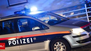 Ein Polizeiauto ist nachts auf einem Parkplatz geparkt. Es hat ein blinkendes Licht oben und eine blau-weiße Farbgebung.