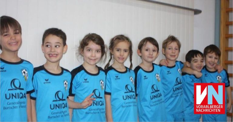 A group of children in matching blue sports jerseys with the word UNIQA on them, standing close together and smiling for a photo.