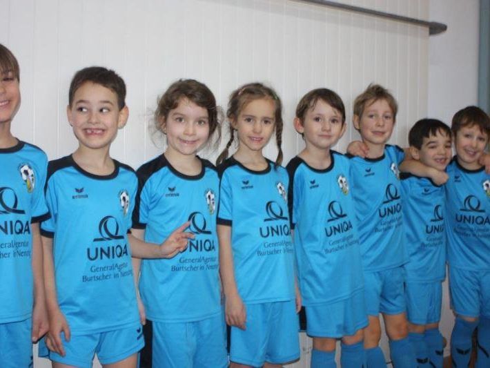 A group of children wearing blue jerseys with white numbers are standing together, smiling and posing for a photo.