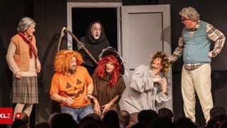 Eine Gruppe von Menschen in Kostümen auf der Bühne, einer hält eine Sense. Das Publikum schaut davor zu.