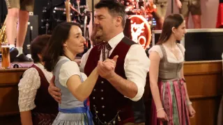Ein Mann und eine Frau tanzen in traditioneller bayerischer Tracht, mit einer Band, die im Hintergrund spielt.