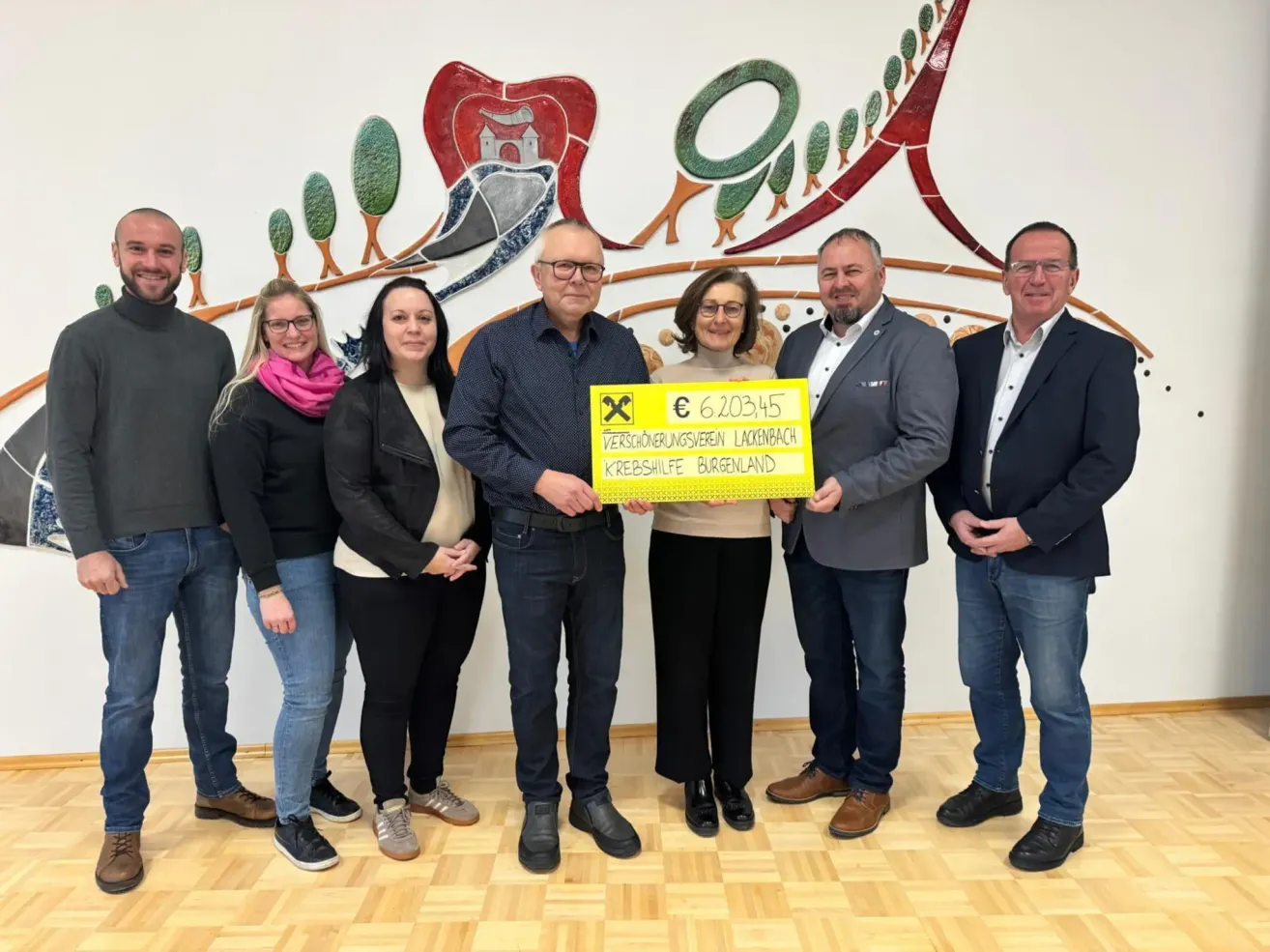 Eine Gruppe von Menschen steht vor einer Wand mit einem gelben Schild und hält einen Scheck über 620345 Euro. Der Scheck ist mit dem Namen eines Sparvereins beschriftet.