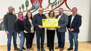 Eine Gruppe von Menschen steht vor einer Wand mit einem gelben Schild und hält einen Scheck über 620345 Euro. Der Scheck ist mit dem Namen eines Sparvereins beschriftet.