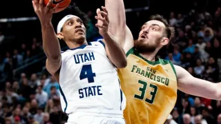 Während eines Basketballspiels versucht ein Spieler von Utah State mit der Trikotnummer 4 zu werfen, während er von einem Spieler aus San Francisco in einem gelben Trikot mit der Nummer 33 blockiert wird.
