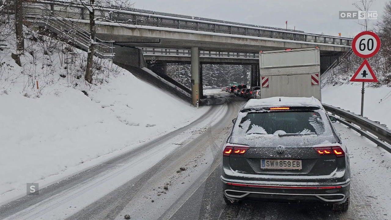 Eine verschneite Straße mit einer Reihe wartender Autos im Verkehr. Eine Brücke ist darüber, und ein Volkswagen Tiguan ist im Vordergrund.