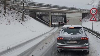 Eine verschneite Straße mit einer Reihe wartender Autos im Verkehr. Eine Brücke ist darüber, und ein Volkswagen Tiguan ist im Vordergrund.