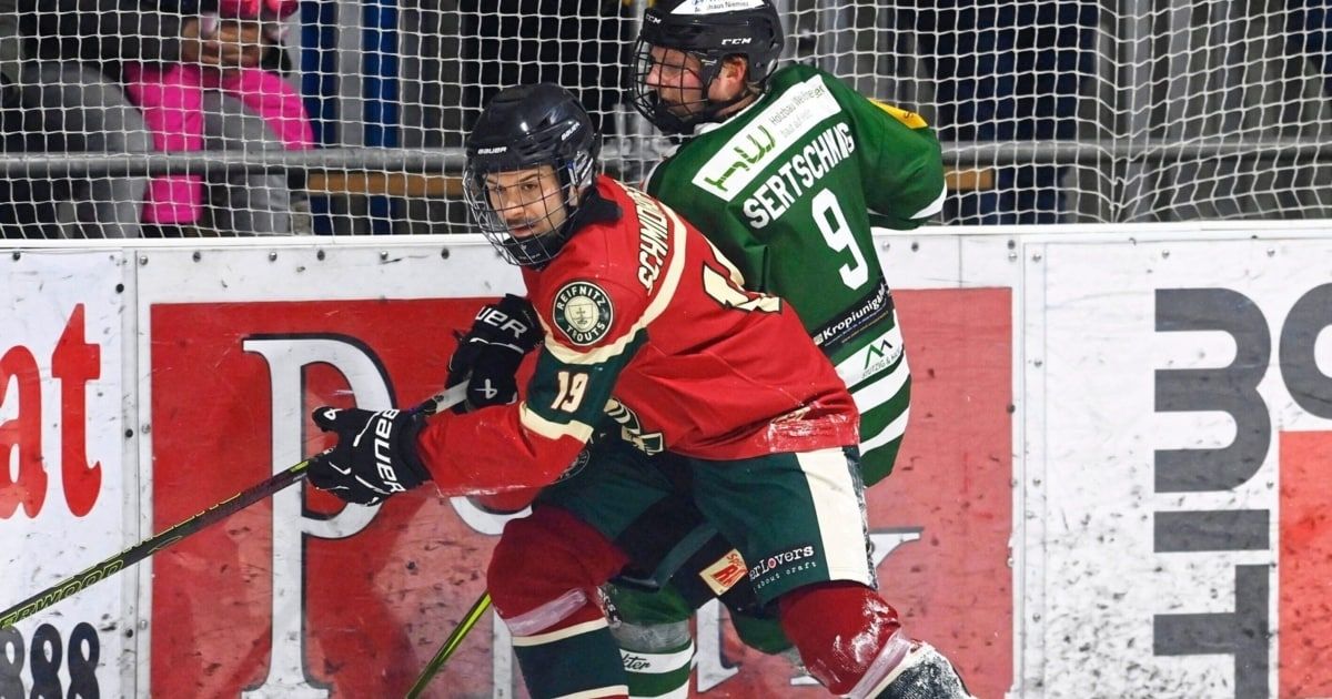 Zwei Eishockeyspieler in roten und grünen Trikots sind auf dem Eis und führen ein Spiel, mit einem unscharfen Hintergrund eines Eishockeyfeldes.