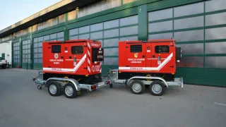 Zwei rote Stroma 45 KVA Generatoren sind nebeneinander vor einem Gebäude mit grünen Türen und Fenstern geparkt.