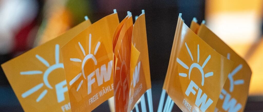 Multiple orange flags with white sun symbols and the letters 'FW' are arranged in a row. The flags are slightly blurred, and the background is dark.