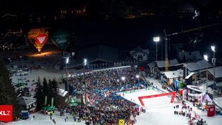 Ein Nachtskievent mit vielen Zuschauern, zwei Heißluftballons und mehreren Fahnen im Hintergrund.