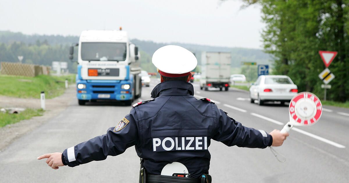 Ein Polizeibeamter regelt den Verkehr auf einer belebten Autobahn, mit mehreren Fahrzeugen, einschließlich Lastwagen, die hinter ihm vorbeifahren.