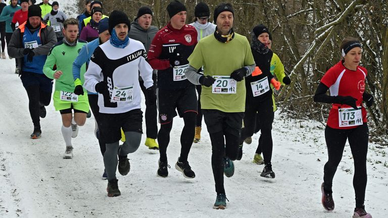 Teilnehmer eines Wintermarathons laufen in einem verschneiten Wald, tragen Winterkleidung und nummerierte Startnummern.