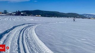 Eine Person treibt Langlauf in einem verschneiten Feld mit klarem blauem Himmel und entfernten Bergen.