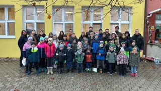 A group of children and adults, dressed in winter clothing, poses for a photo in front of a yellow building with large windows.