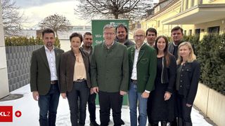 A group of people, possibly employees, are standing in a line for a photograph in the snow. They are wearing formal clothing. Behind them is a building with a signboard.