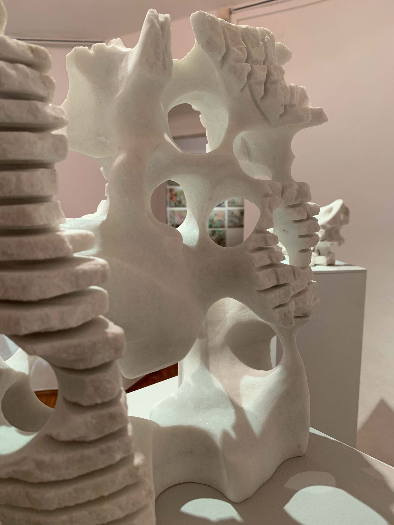 Eine Nahaufnahme einer weißen Skulptur, die einer Knochenstruktur mit mehreren Löchern und einer Reihe gestapelter zylindrischer Formen ähnelt. Die Skulptur steht auf einem weißen Sockel.