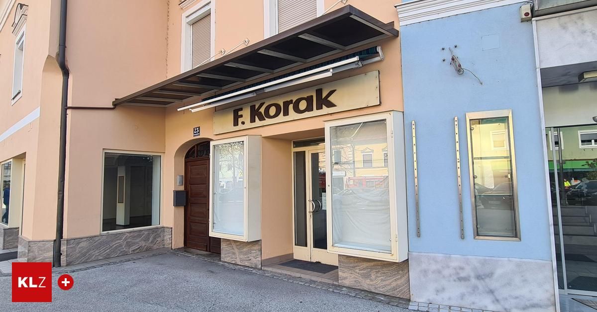 Ein Bild eines Gebäudes mit dem Schild F. Korak. Der Eingang hat zwei Glastüren, mit einem Teppich auf dem Boden. Die Fenster sind mit Glas und Holzläden verdeckt.