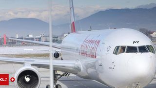 An Austrian Airlines jet is parked on the runway with snowy mountains in the background.