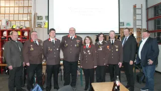 A group of people in uniform standing in front of a projector screen with a presentation. They are all smiling and seem to be posing for a photo.