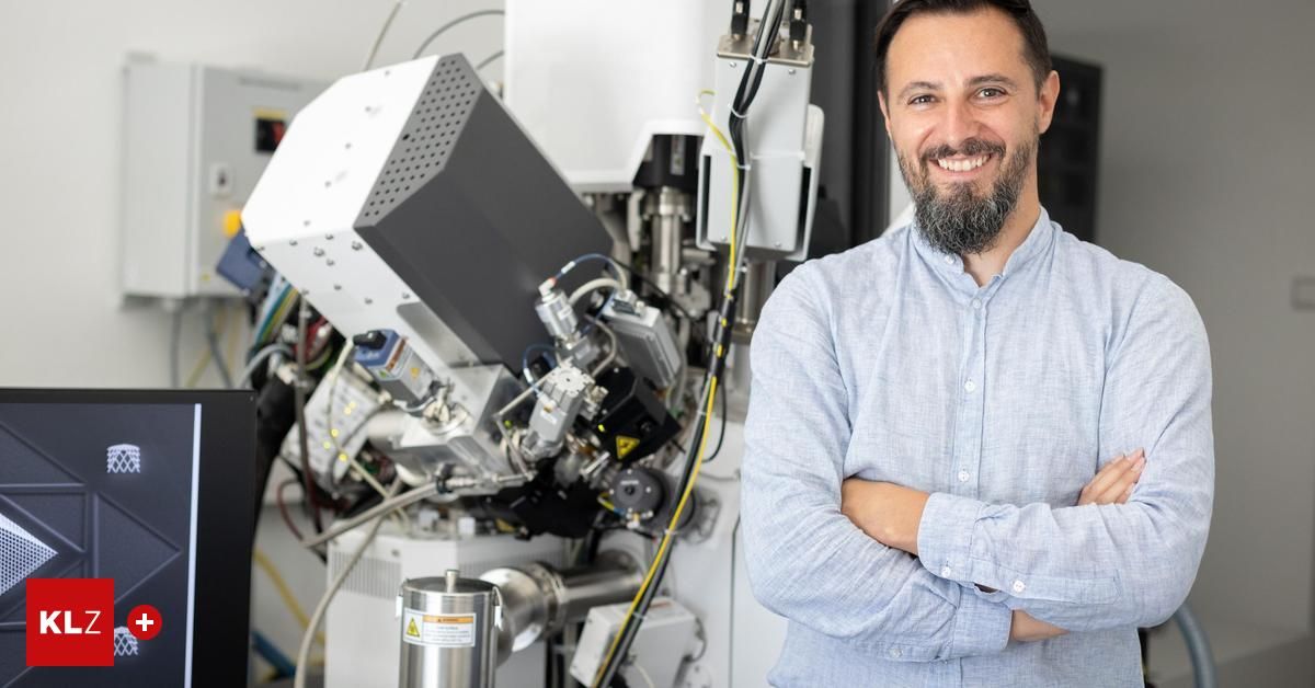 A man in a light blue shirt is standing next to a large machine with wires and metal parts.
