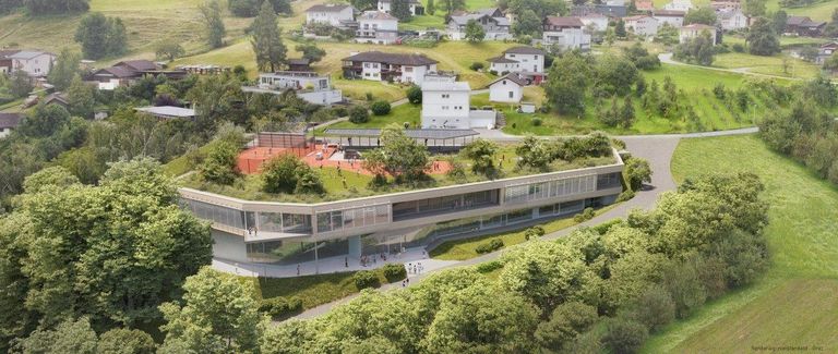 Eine Luftaufnahme eines modernen Gebäudes mit grünem Dach, umgeben von Bäumen und Häusern. Das Gebäude hat Glasfenster und einen Tennisplatz auf dem Dach. Es gibt Menschen, die in der Gegend herumlaufen.