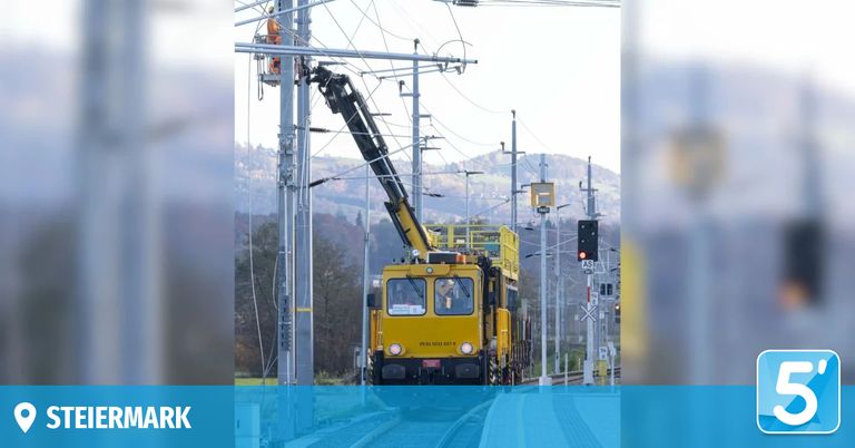 Ein gelber Zug auf Schienen mit einem Kran oben, einem Arbeiter in einem Korb und einer roten Signalleuchte.