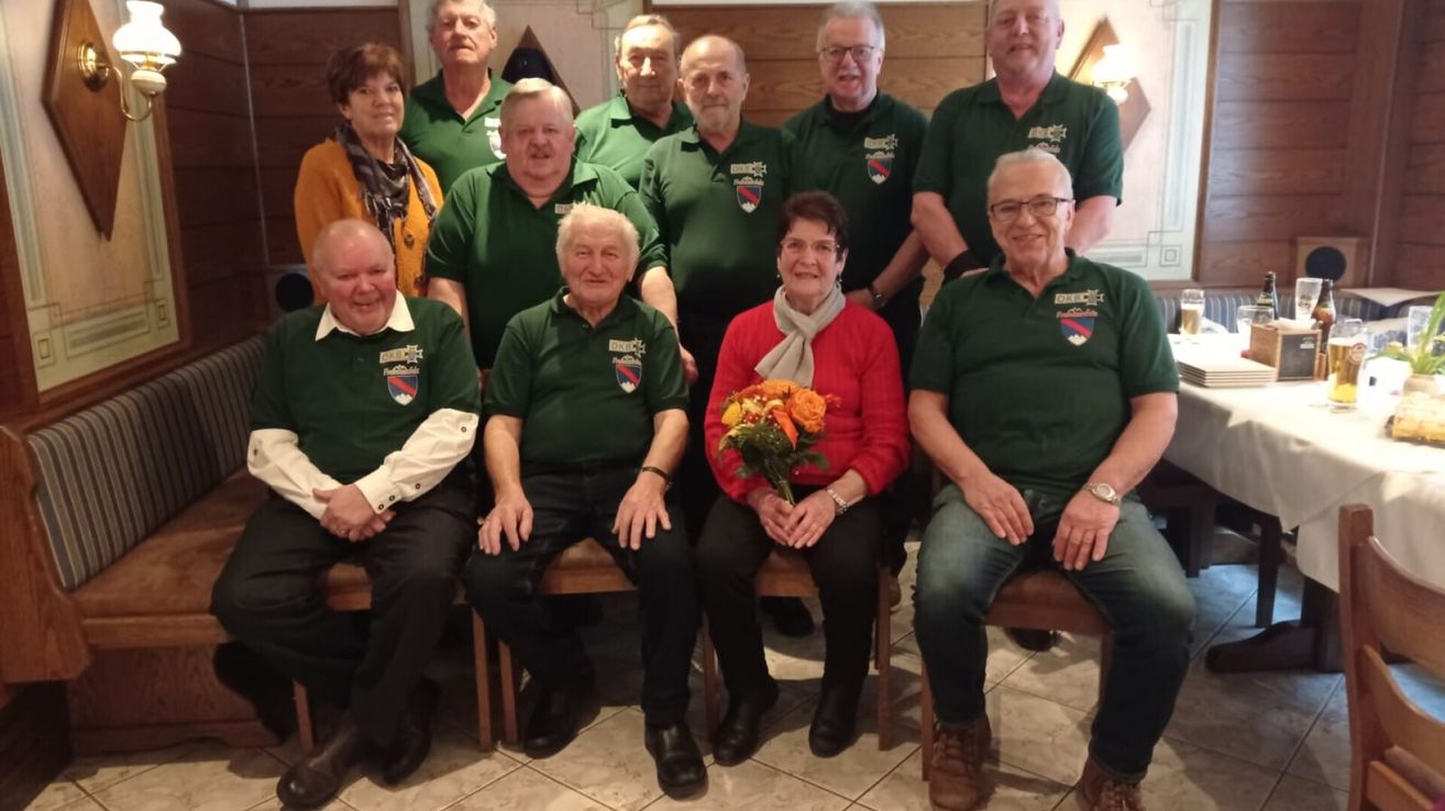 Eine Gruppe von Menschen in grünen Poloshirts posiert für ein Foto mit einer Frau, die Blumen in der Mitte hält.