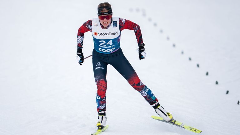 Eine Langläuferin mit der Nummer 24 auf ihrem Outfit rennt einen verschneiten Hang hinunter, mit Schutzbrille und Stirnband.