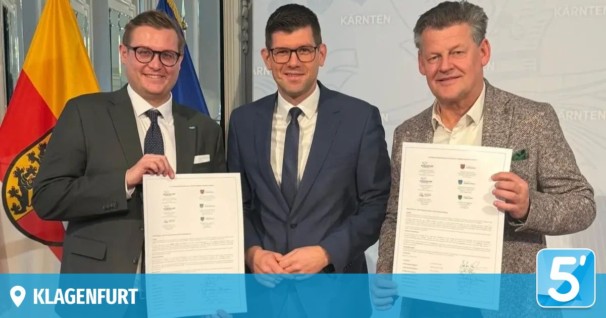 Drei Männer in Anzügen halten Urkunden in den Händen, lächeln und stehen vor einem weißen Hintergrund mit dem Wort 'Karnten'. Der Mann auf der linken Seite trägt eine Brille und eine Krawatte.