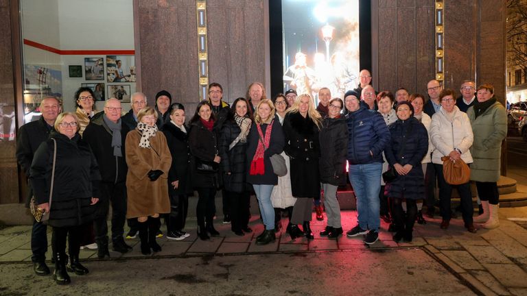 Eine Gruppe von Menschen in Winterkleidung steht vor einem Gebäude mit einem großen Fenster, das von roten Lichtern beleuchtet wird.