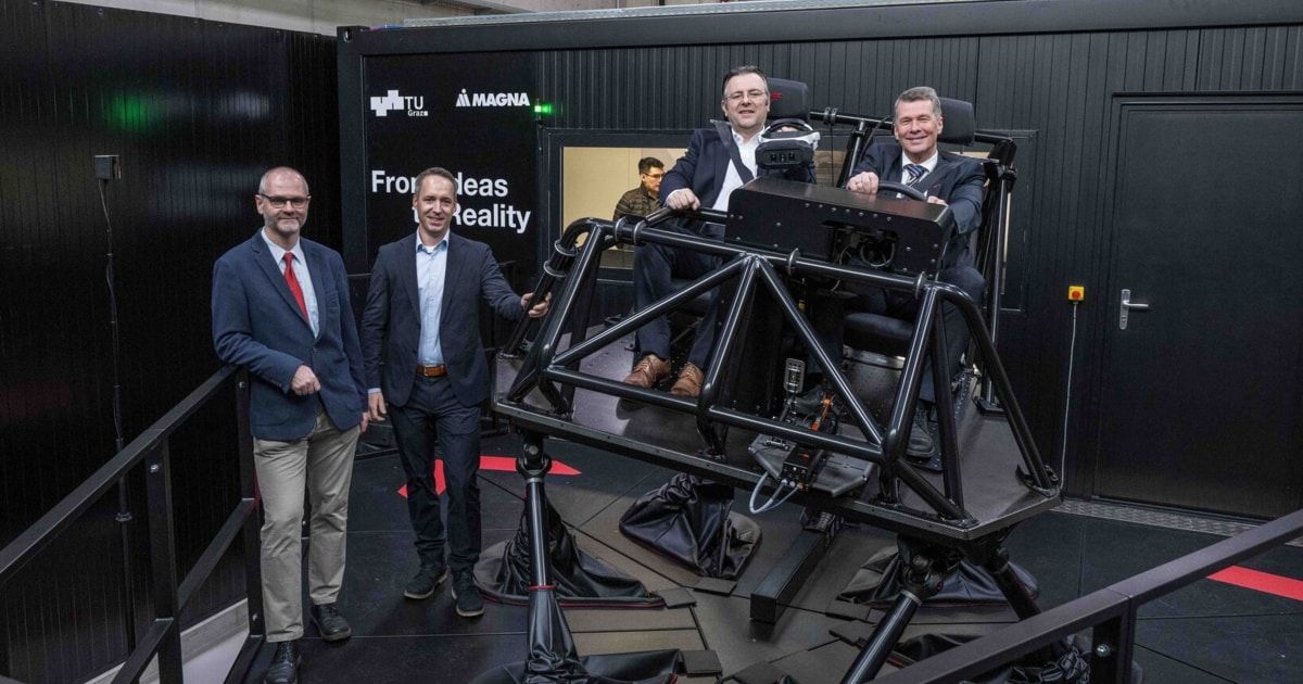 Vier Männer in Anzügen stehen um ein Fahrzeug herum, in dem zwei Männer sitzen. Dahinter befindet sich eine große Leinwand mit dem Text 'Von der Idee zur Realität'.