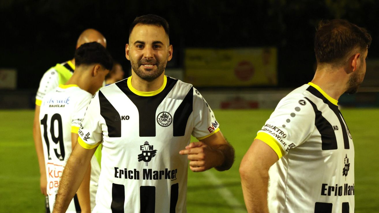 Ein Fußballspieler in einem weiß-schwarz gestreiften Trikot mit der Aufschrift 'Erich Marker' lächelt und blickt nach rechts. Dahinter stehen zwei weitere Spieler.