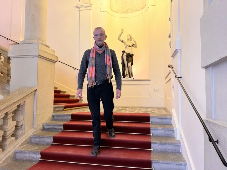 Ein Mann mit Schal geht eine Treppe in einem Gebäude mit einer Statue an der Wand hoch.