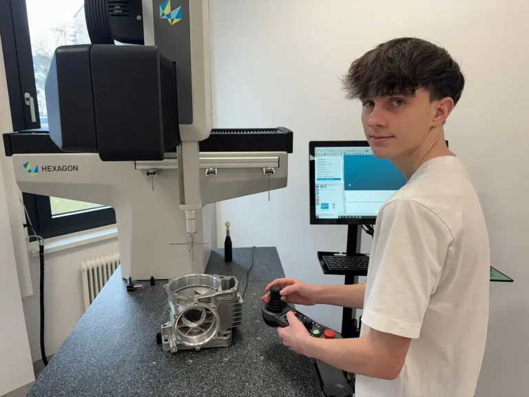 Ein junger Mann bedient eine Maschine in einem Labor. Er hält einen Controller und konzentriert sich auf den Bildschirm, der Daten anzeigt.