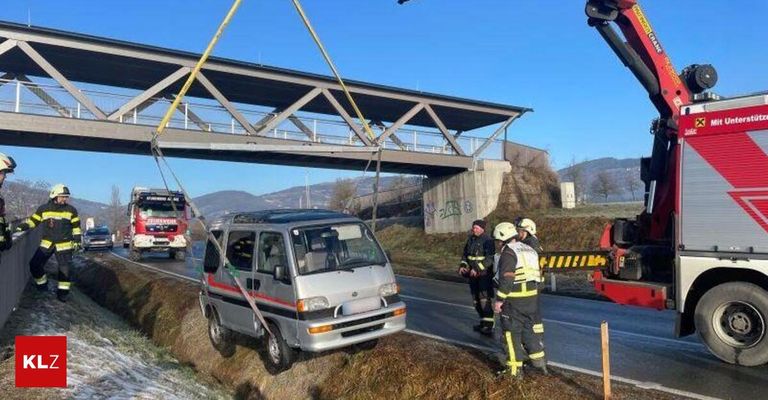 Ein Kleintransporter wird von einem Kran auf der Straßenseite angehoben. Zwei Feuerwehrleute stehen in der Nähe. Eine Brücke befindet sich über dem Van.