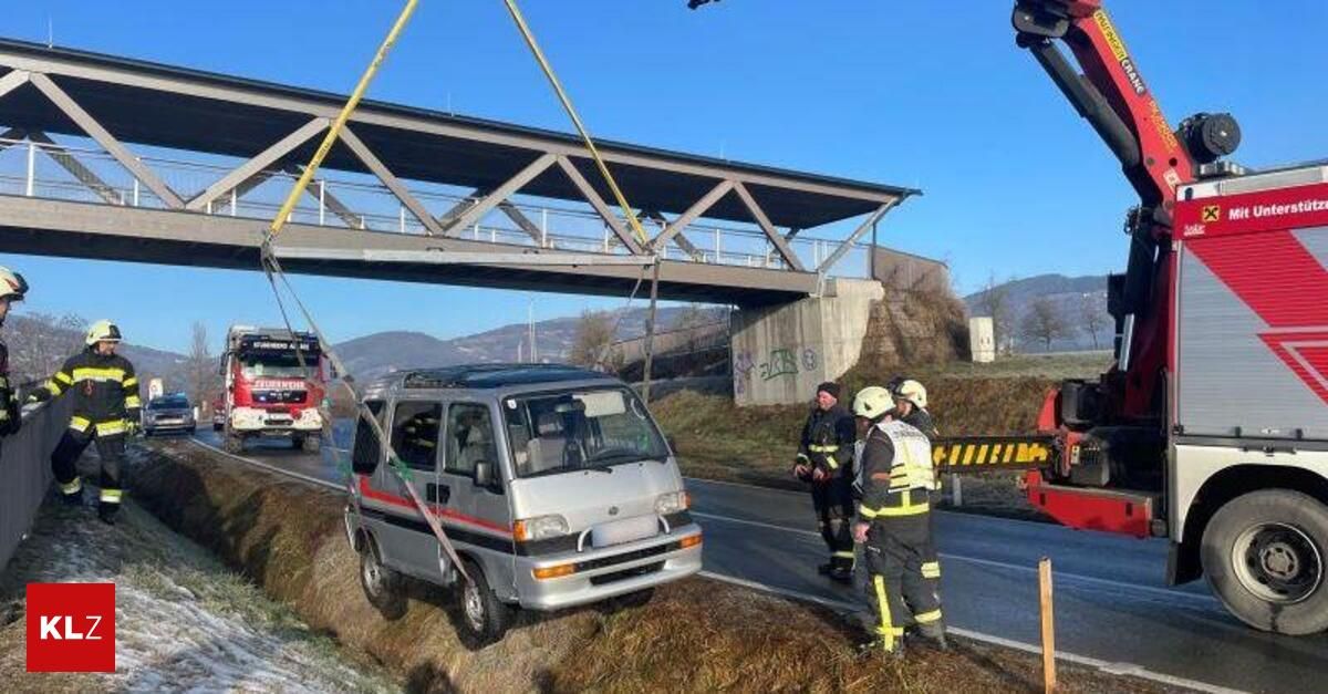 Ein Kleintransporter wird von einem Kran auf der Straßenseite angehoben. Zwei Feuerwehrleute stehen in der Nähe. Eine Brücke befindet sich über dem Van.