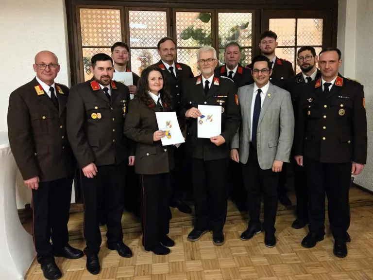 Eine Gruppe von Militärangehörigen in Uniform steht in einem Raum, wobei ein Mann in der Mitte ein Papier hält, während andere lächeln und zur Kamera schauen.