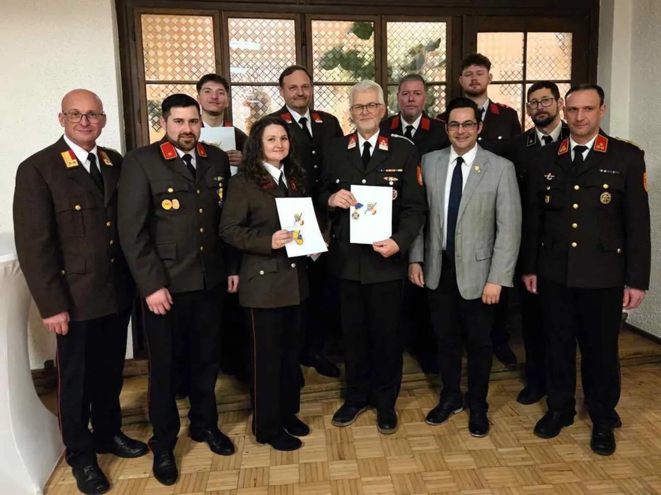 Eine Gruppe von Militärangehörigen in Uniform steht in einem Raum, wobei ein Mann in der Mitte ein Papier hält, während andere lächeln und zur Kamera schauen.