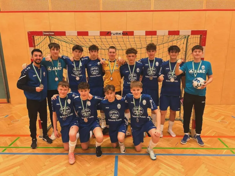 Eine Gruppe junger Athleten mit Medaillen posiert für ein Foto vor einem Handballtor.