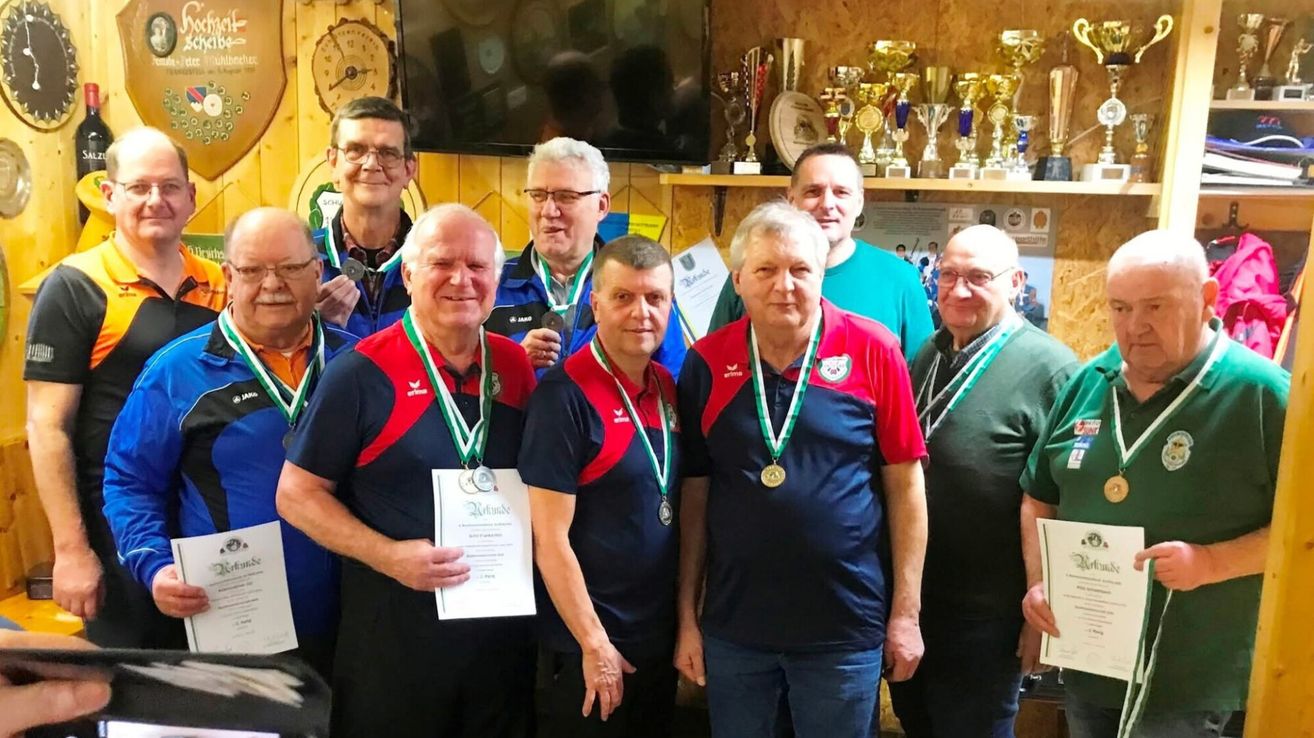 Eine Gruppe von Männern mit Medaillen posiert für ein Foto vor einem Regal mit Trophäen. Sie haben Lächeln auf ihren Gesichtern.