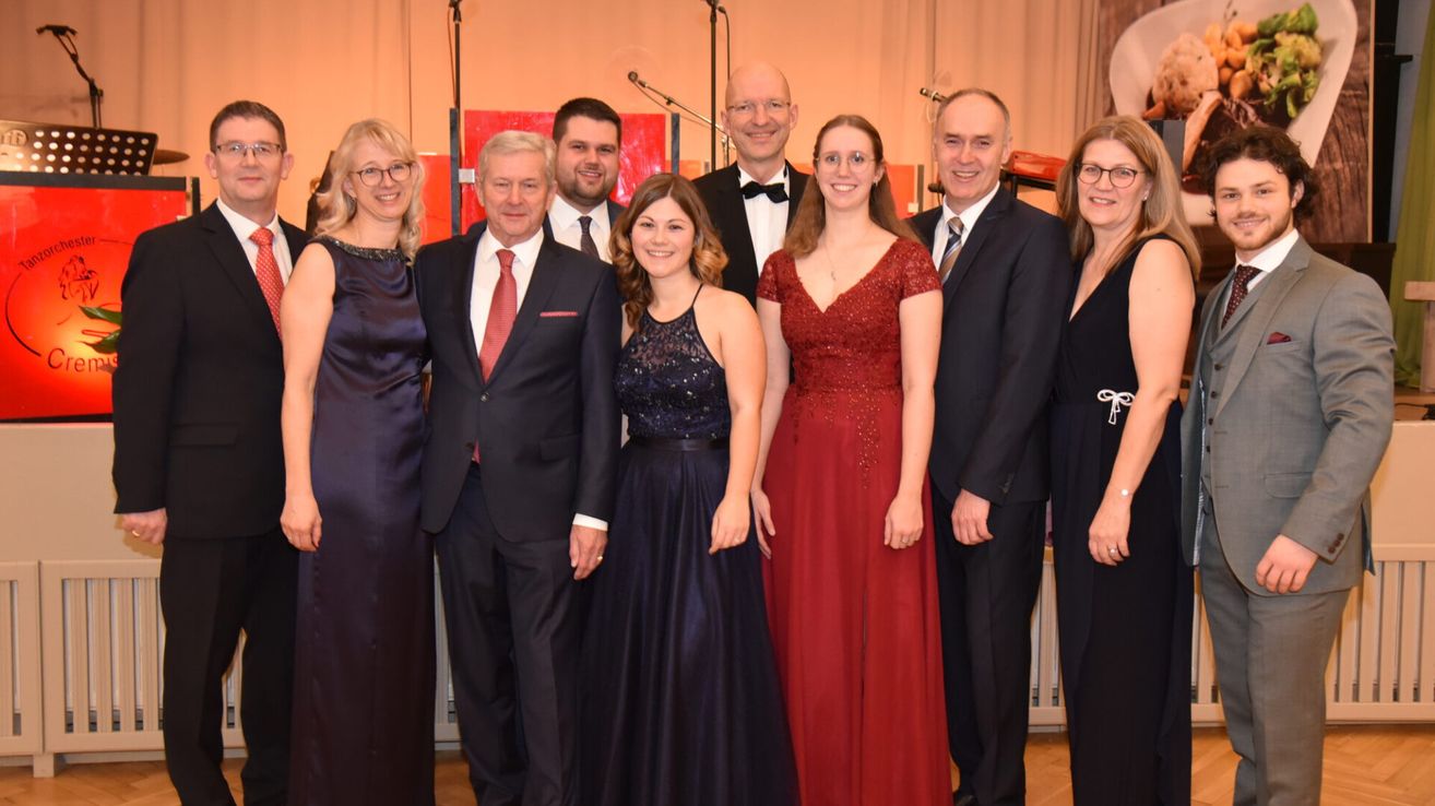 Eine Gruppe formell gekleideter Personen posiert für ein Foto, möglicherweise bei einer Preisverleihung, mit einem warmen Hintergrund und Bühnenaufbau.