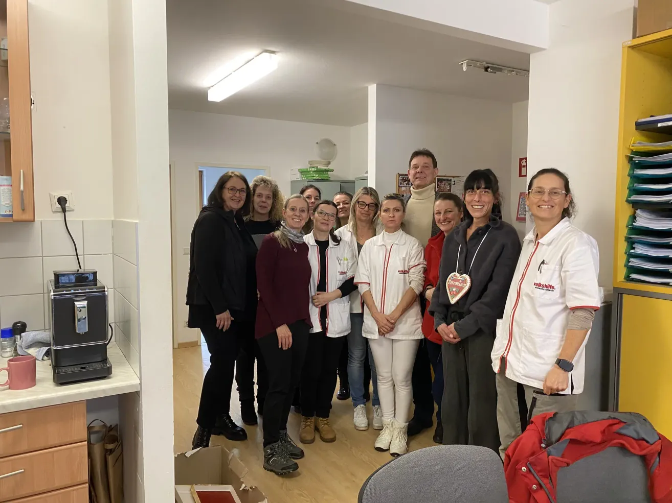 Eine Gruppe von Frauen und Männern in weißen Kitteln und Brillen steht in einem Raum mit Holzböden und weißen Wänden.