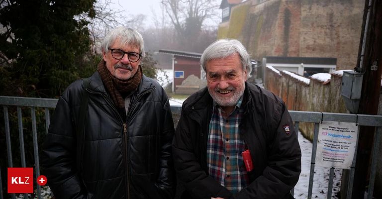 Zwei ältere Männer, die lächeln und vor einer verschneiten Kulisse stehen. Beide tragen Jacken.