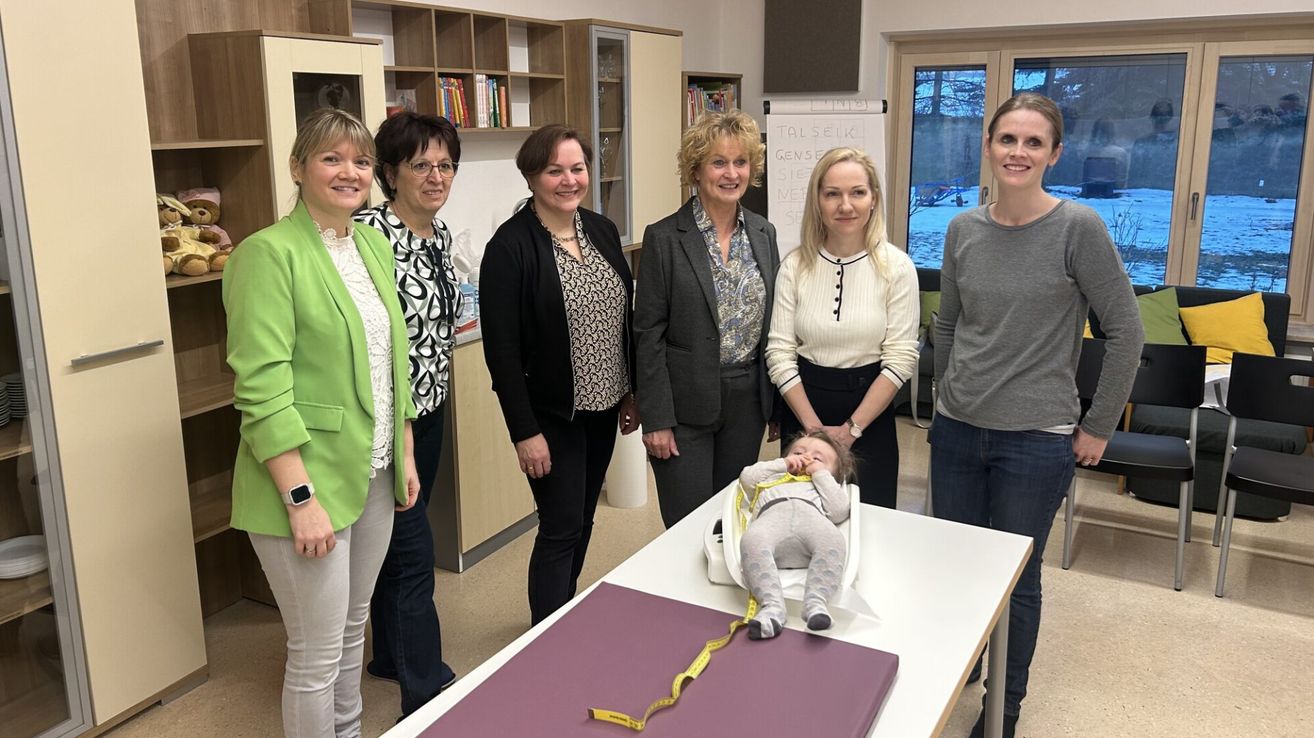 Fünf Frauen und ein Baby in einem Stuhl. Eine Frau misst die Größe des Babys mit einem Maßband.