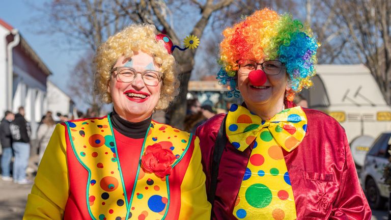 Zwei Frauen, verkleidet als Clowns, lächeln in die Kamera. Sie sind draußen, mit einem Baum und einem unscharfen Publikum im Hintergrund.