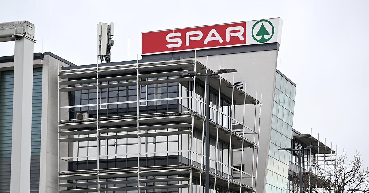 Ein modernes Gebäude mit einem roten und weißen Schild, auf dem SPAR steht, umgeben von Gerüsten. Das Gebäude hat Glasfenster und eine Klimaanlage.