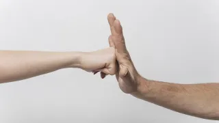 Zwei Hände sind ineinander verschränkt, eine Hand von einer Person auf der linken Seite und die andere von einer Person auf der rechten Seite.