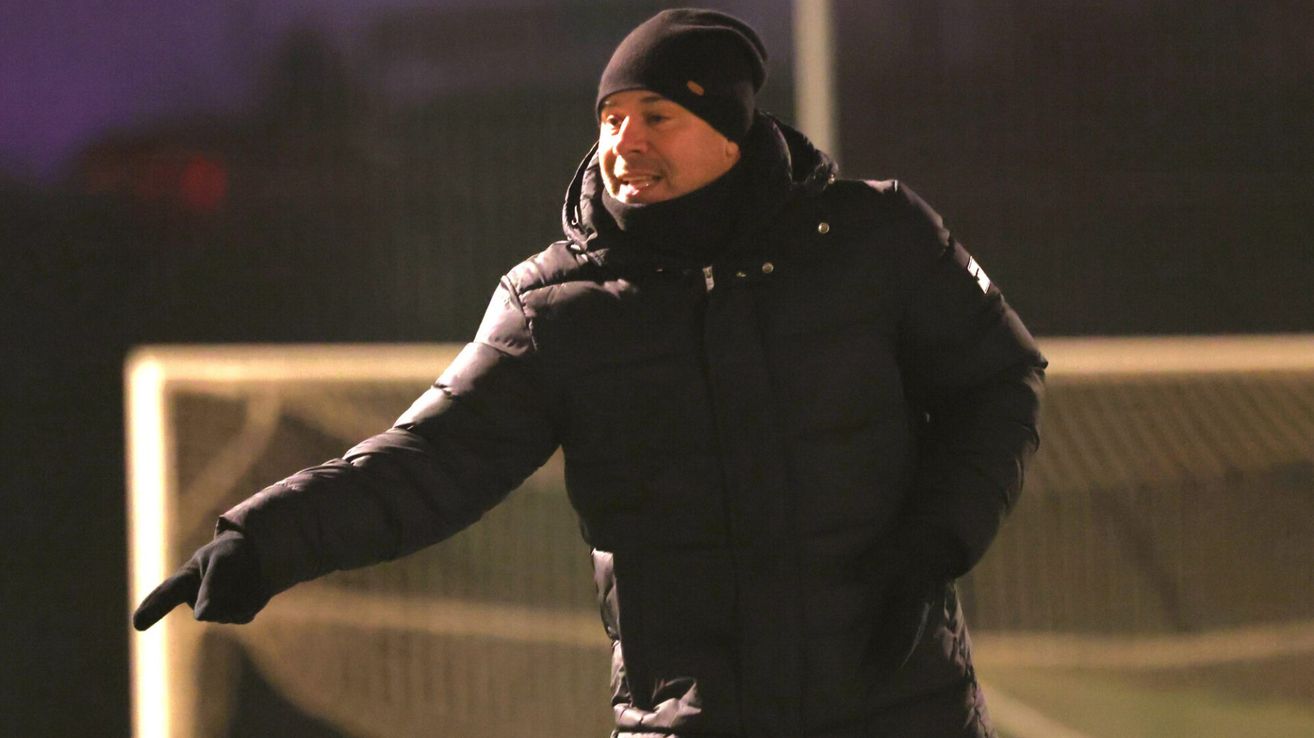 Ein Mann in einer schwarzen gepolsterten Jacke und Mütze läuft bei Nacht auf einer nassen Straße. Er hat ein Lächeln im Gesicht.