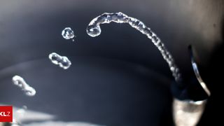Eine Nahaufnahme von Wassertropfen, die aus einem Wasserhahn fließen, aufgenommen mit geringer Schärfentiefe.